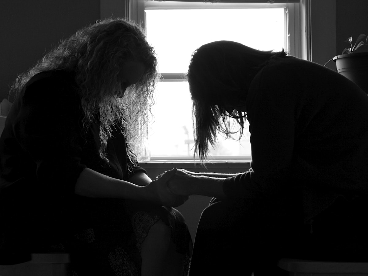 Two people sitting and holding hands while praying together