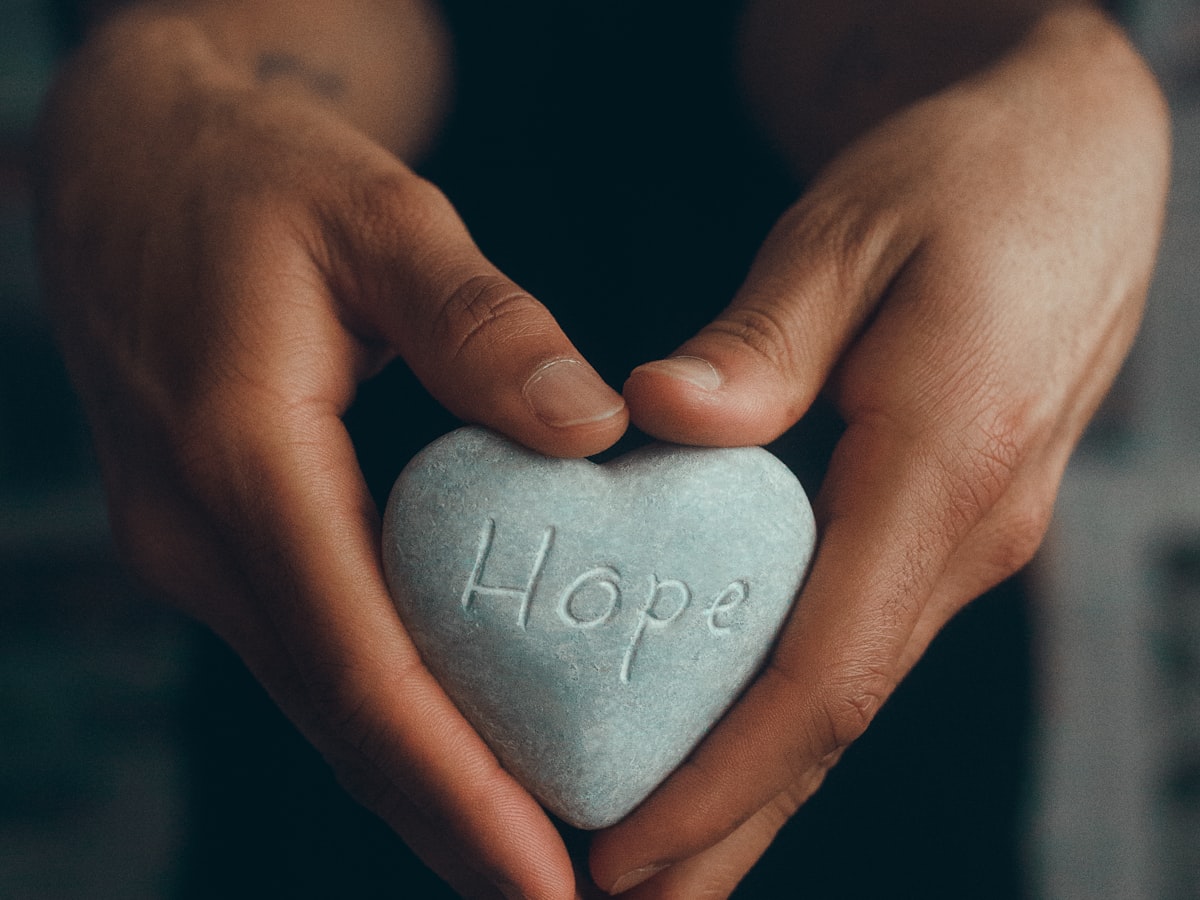 Hands holding a stone heart engraved with the word Hope